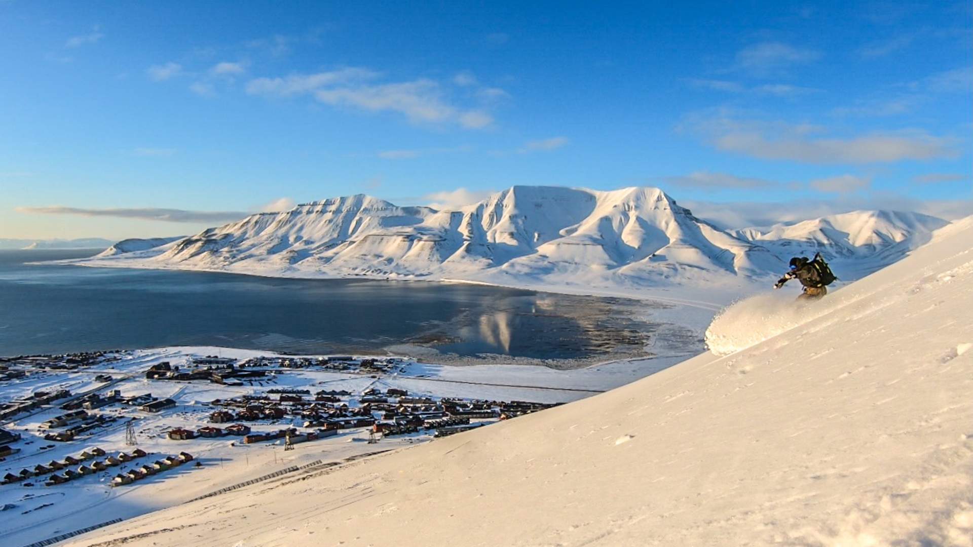 a man skiing down a hill overviewing a fjord of Svalbard